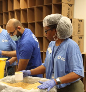 Monica Council-Miles holds a scoop as she preps to pour soy into into a Rise Hunger meal bag through a yellow funnel.